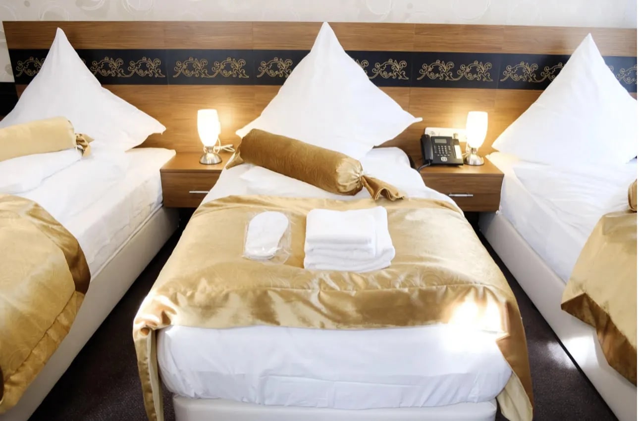 Dreibettzimmer mit drei Betten, goldenen Tagesdecken und Leselampen