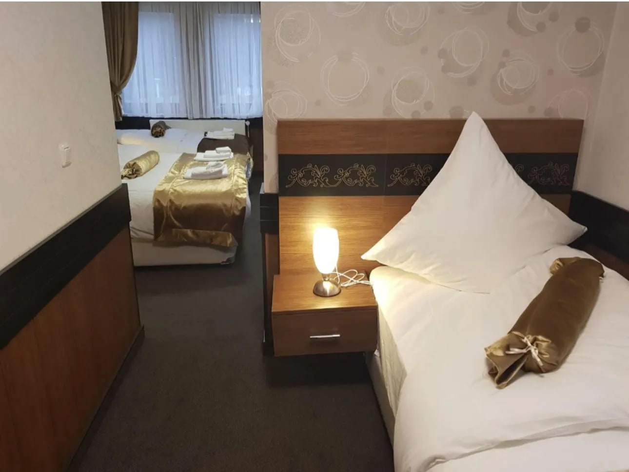 Einzelbett mit Nachttischlampe, weitere Betten im Spiegel sichtbar